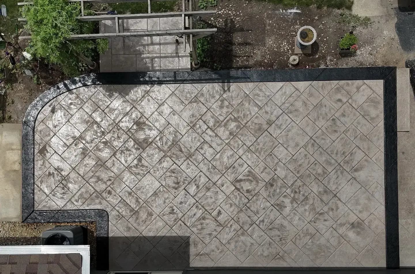 Overhead view of a stamped concrete patio in a diagonal tile pattern with a dark border band